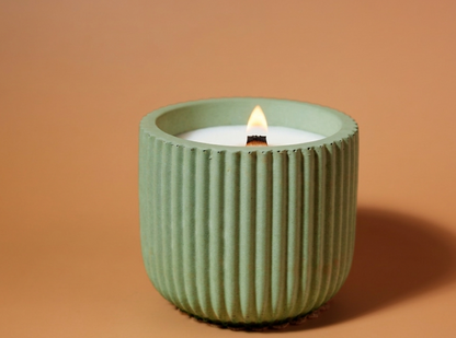 A lit candle in a ribbed, light sage green ceramic holder, set against a solid warm terracotta background.