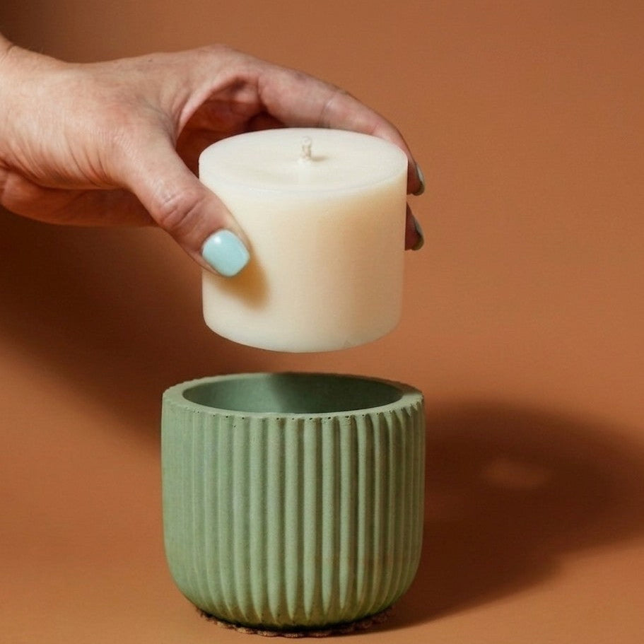 Hand holding a white candle above a green textured pot on a brown background